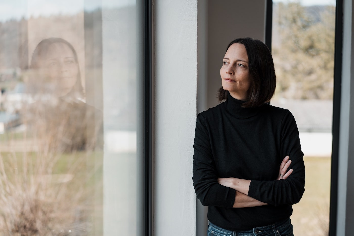 a serious woman in black thinks as she looks out a window