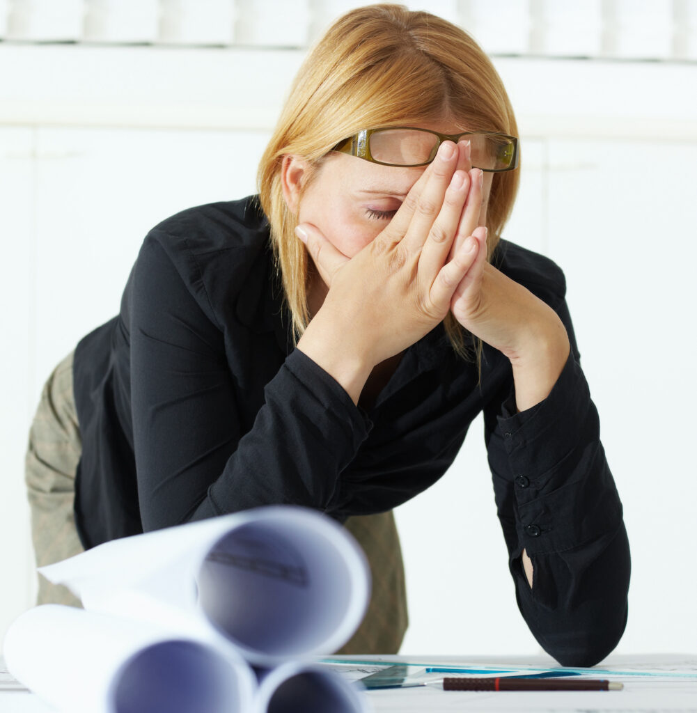 stressed female architect has head in hands leaning over architectural drawings