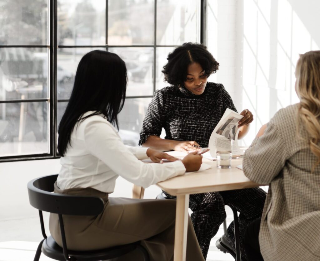 three women sit at a table reviewing documents